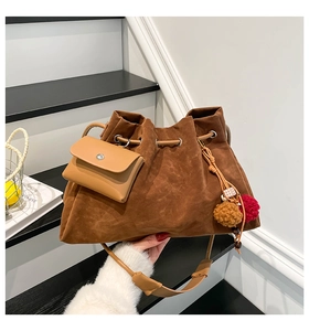 Detail of vintage brown suede bucket bag with colorful pom-pom charm on stairs
