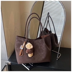 Detail of vintage brown suede tote bag with a cute teddy bear charm in a lifestyle setting