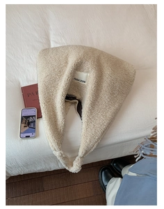 Detailed texture of beige faux shearling tote bag with SEEYOU label on a cozy bed