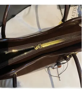 Detail view of smooth metal gold zipper and rich brown leather texture on tote bag