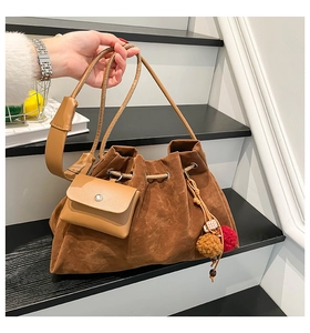 Detail of a brown suede bucket bag with drawstring closure and colorful pompom charm