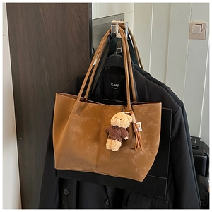 Detail of brown suede tote bag featuring a teddy bear charm and vertical seam design