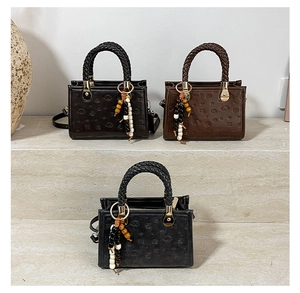 Detail of vintage tote bags with embossed patterns and woven handles on a stone pedestal