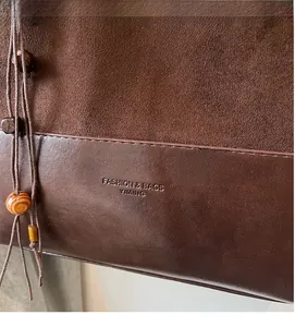 Detail of dark brown suede and leather bucket bag with debossed logo and wooden bead tassel