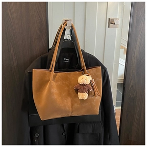 Close-up of brown suede tote bag featuring fine stitching and a cute teddy bear charm