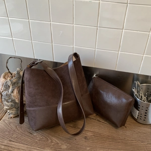 Detail of dark brown matte leather tote bag with matching zippered pouch on wooden table