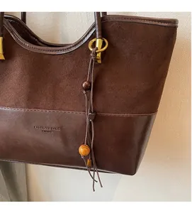 Detail of faux suede and leather contrast stitching on a dark brown bucket bag with beads