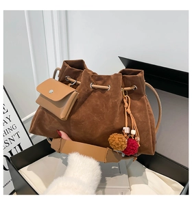 Detail of dark brown suede bucket bag featuring drawstring closure and plush pendant