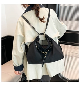 Rear view of a minimalist black multifunctional backpack worn over a beige trench coat