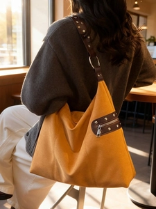Large mustard yellow suede shoulder bag with studded brown strap in a cafe setting