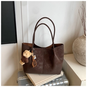 Close-up of a large brown suede tote bag with a cute teddy bear charm on a suitcase