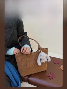 Nahaufnahme der braunen Shopper-Tasche aus Kunstleder mit Plüschhasen-Anhänger und Ahornblatt