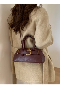 Deep burgundy retro bag with gold metal buckle detail on beige wool coat background