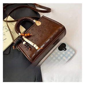 Close-up of brown leather bag with embossed dog motifs and woven handle with bead charm