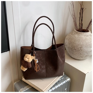 Detail of vintage brown faux suede tote bag with plush bear charm on suitcase