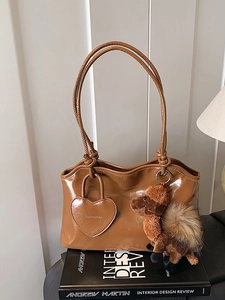 Borsa tote in pelle lucida caramello con ciondolo a cammello posata su libri