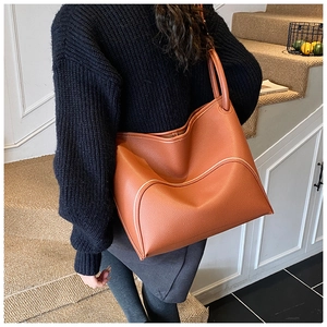 Brown leather tote bag showing large capacity and contrast stitching detail on model