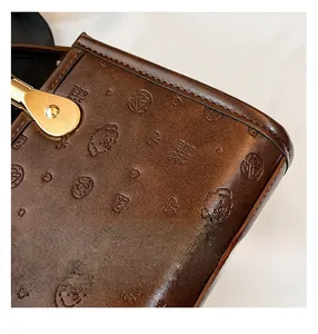 Detail of dark brown leather bag with dog embossing and premium gold hardware