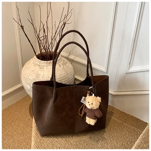 Detail of dark brown suede tote bag with cute teddy bear charm and long shoulder strap
