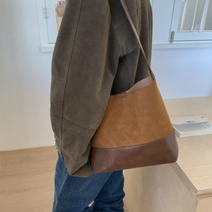 Detail of suede and leather bucket bag worn over shoulder in minimalist interior