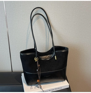 Detail of minimalist black tote bag with suede and leather patchwork and tassel charm