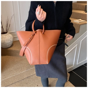 Detail of tan lychee grain leather bucket bag with white contrast stitching and round handle