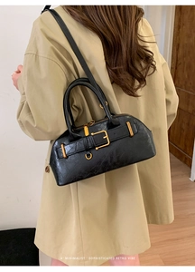Minimalist black retro shoulder bag with gold hardware shown on a model in a trench coat