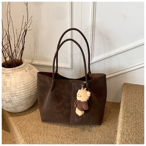 Detail of a dark brown suede tote bag featuring a cute teddy bear plush charm hanging on it