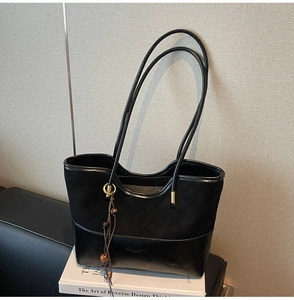 Close-up of black crossbody tote bag with suede contrast, gold rings and beaded tassel