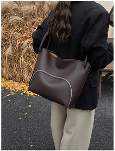 Detail of dark brown pebble leather tote bag featuring contrast white piping in autumn setting