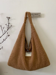 Brown faux shearling tote bag with SEEYOU label hanging on a minimal wall with branch decor