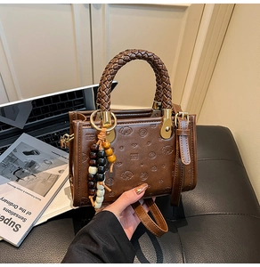 Detailed close-up of brown embossed tote bag with woven handles and colorful bead charm