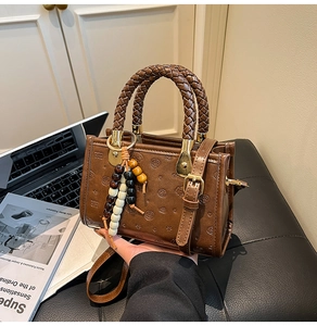 Detail of a brown textured crossbody bag with woven handles and ethnic wooden beads