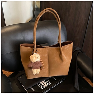 Detail of vintage brown suede tote bag with plush bear charm on black leather chair
