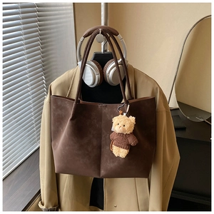 Detailed close-up of a vintage brown suede tote bag featuring contrast stitching and bear charm