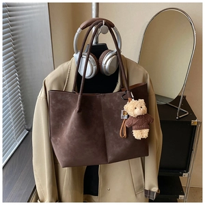 Detail of dark brown faux suede tote bag featuring a cute teddy bear charm and long strap