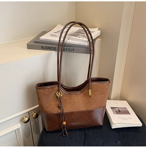 Detail of a brown patchwork tote bag with suede texture and decorative fringe tassels