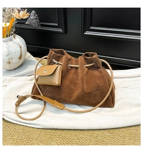 Detail of a brown suede drawstring bucket bag with pleats and a small tan accessory pouch