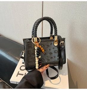 Detail of black crossbody bag featuring embossed cartoon motifs and woven leather handles