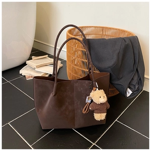 Detail of dark brown suede tote bag with slim handles and a cute teddy bear charm