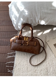 Close-up of brown textured leather handbag with gold buckle and retro belt detailing