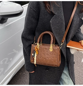 Detail of dark brown leather handbag with embossed cartoon pattern and woven handle