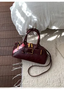 Detail of burgundy leather boston bag showing vintage brass buckle and shiny texture