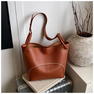 Detailed close-up of brown bucket bag with white contrast piping on textured leather