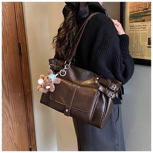 Detail of dark brown vintage tote bag with side buckles and a cute teddy bear charm