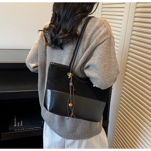 Detail of black tote bag featuring a suede texture contrast with ethnic tassel charm