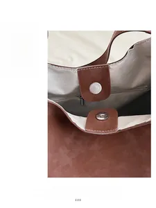 Detail view of the magnetic closure and herringbone fabric lining on a brown suede tote bag