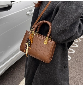 Detailed view of brown embossed handbag with woven handle and colorful beaded charm