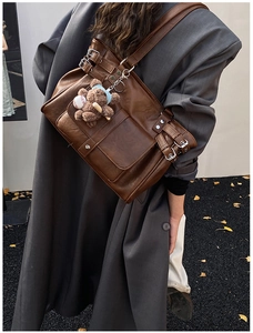 Detail of dark brown vintage tote bag with buckle straps and plush bear charm on a shoulder
