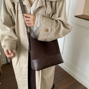 Detail of vintage dark brown crossbody bucket bag worn with a khaki trench coat